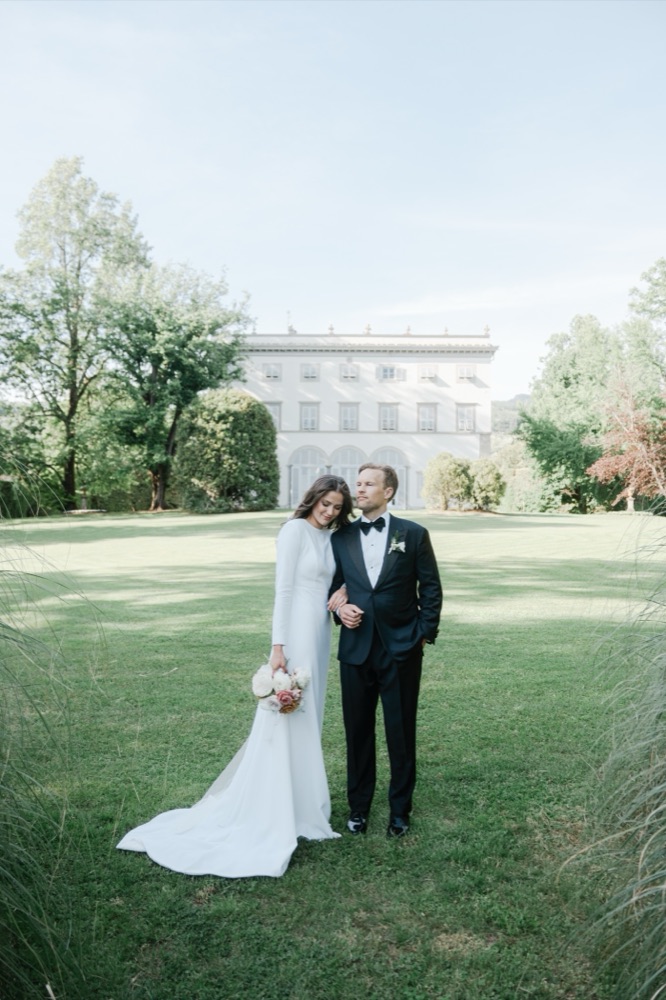 Bride and groom arm in arm on the lawn in front of a grand Tuscan villa