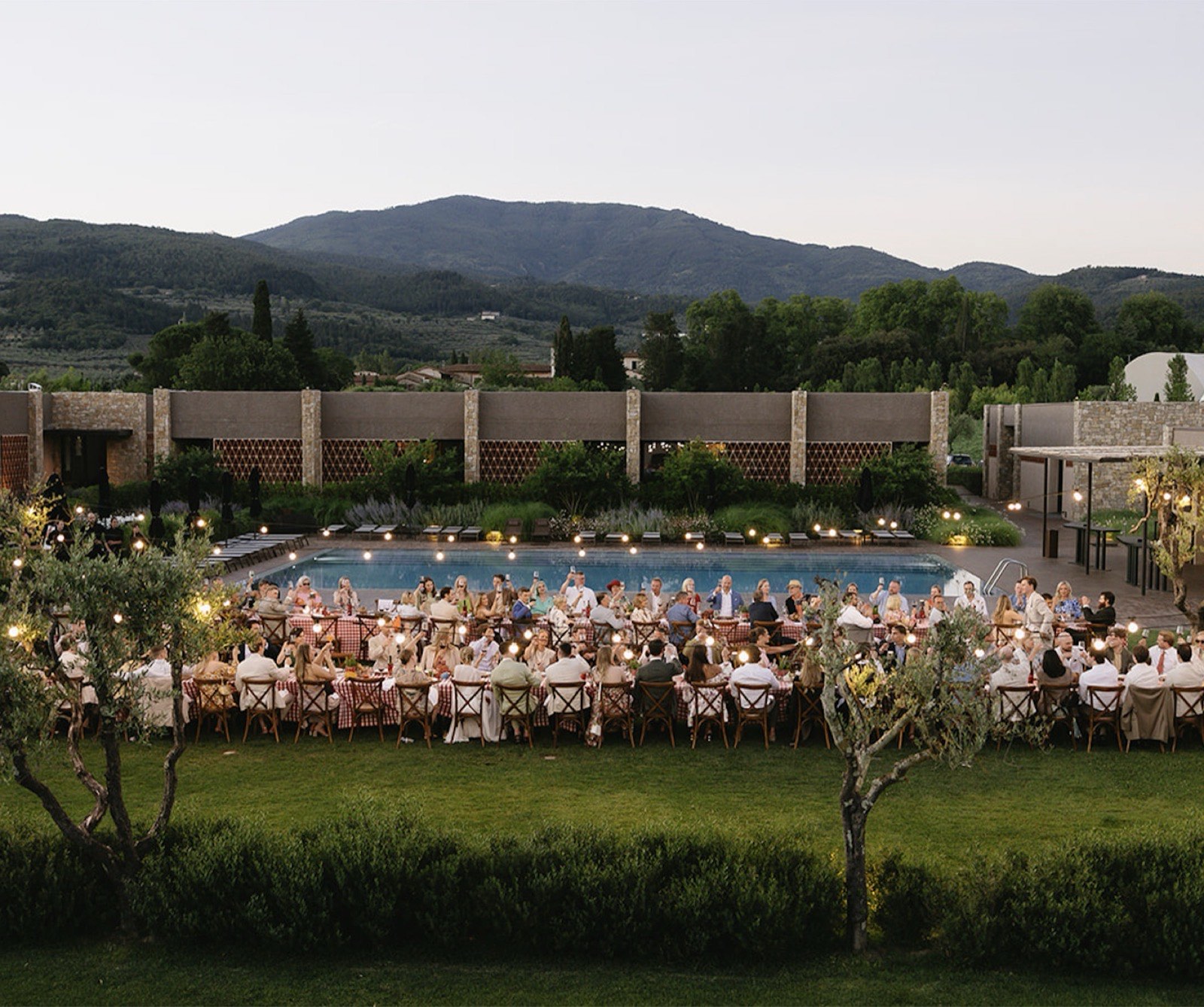 Long poolside dinner reception at dusk with string lights and mountains in the background
