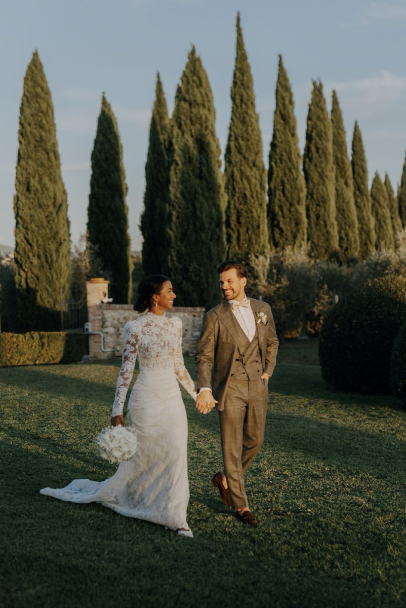 Isatou and Sami walking hand in hand through a cypress-lined Tuscan garden