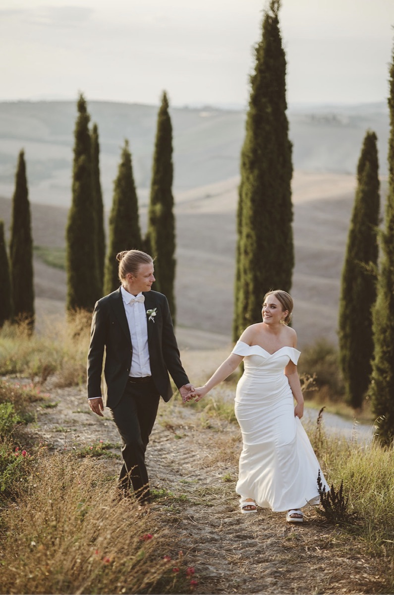 Kaisa and Paavo walking hand in hand along a cypress-lined path in the Tuscan hills