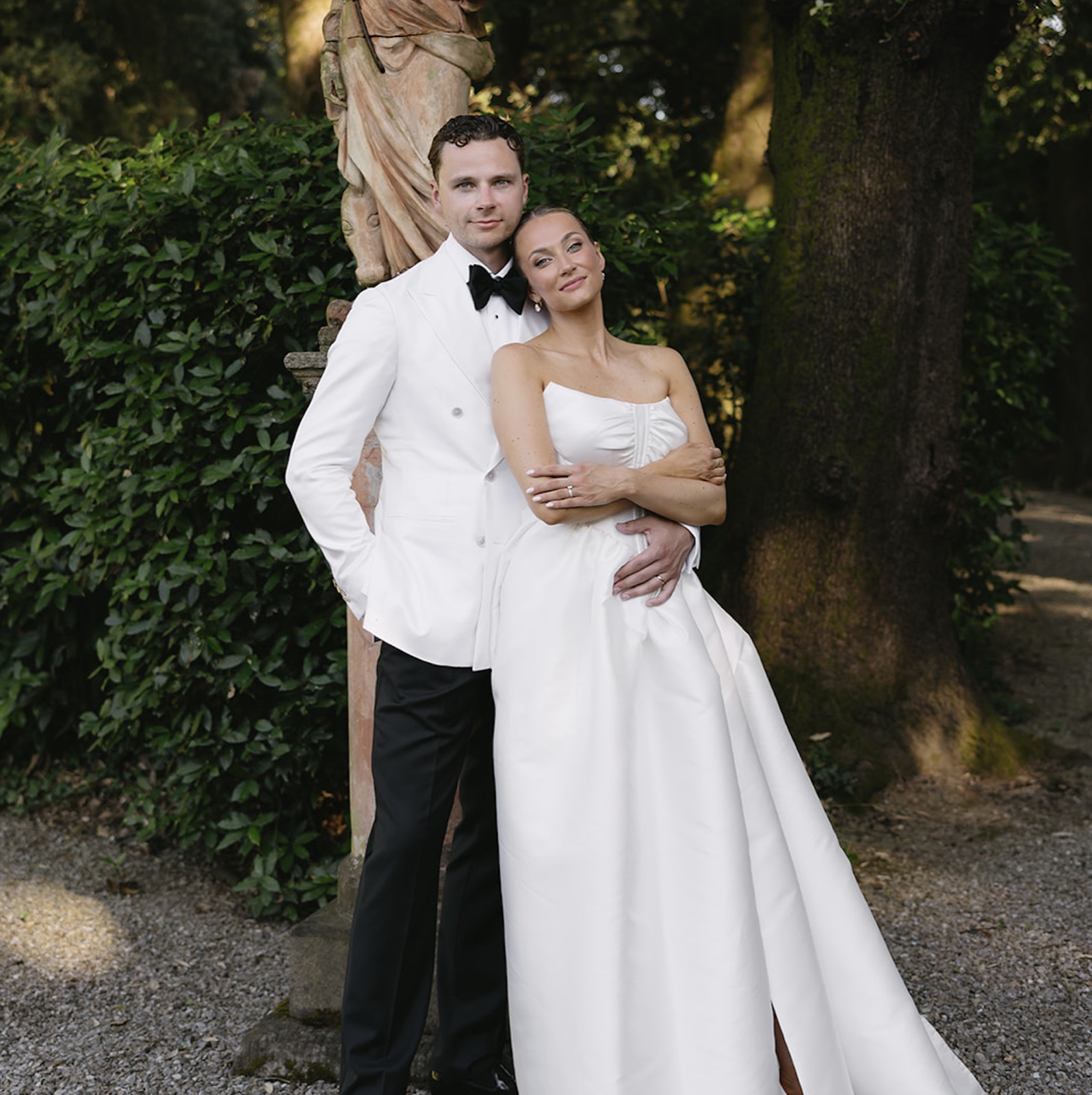 Freja and Daniel embracing in front of a garden statue beneath the trees