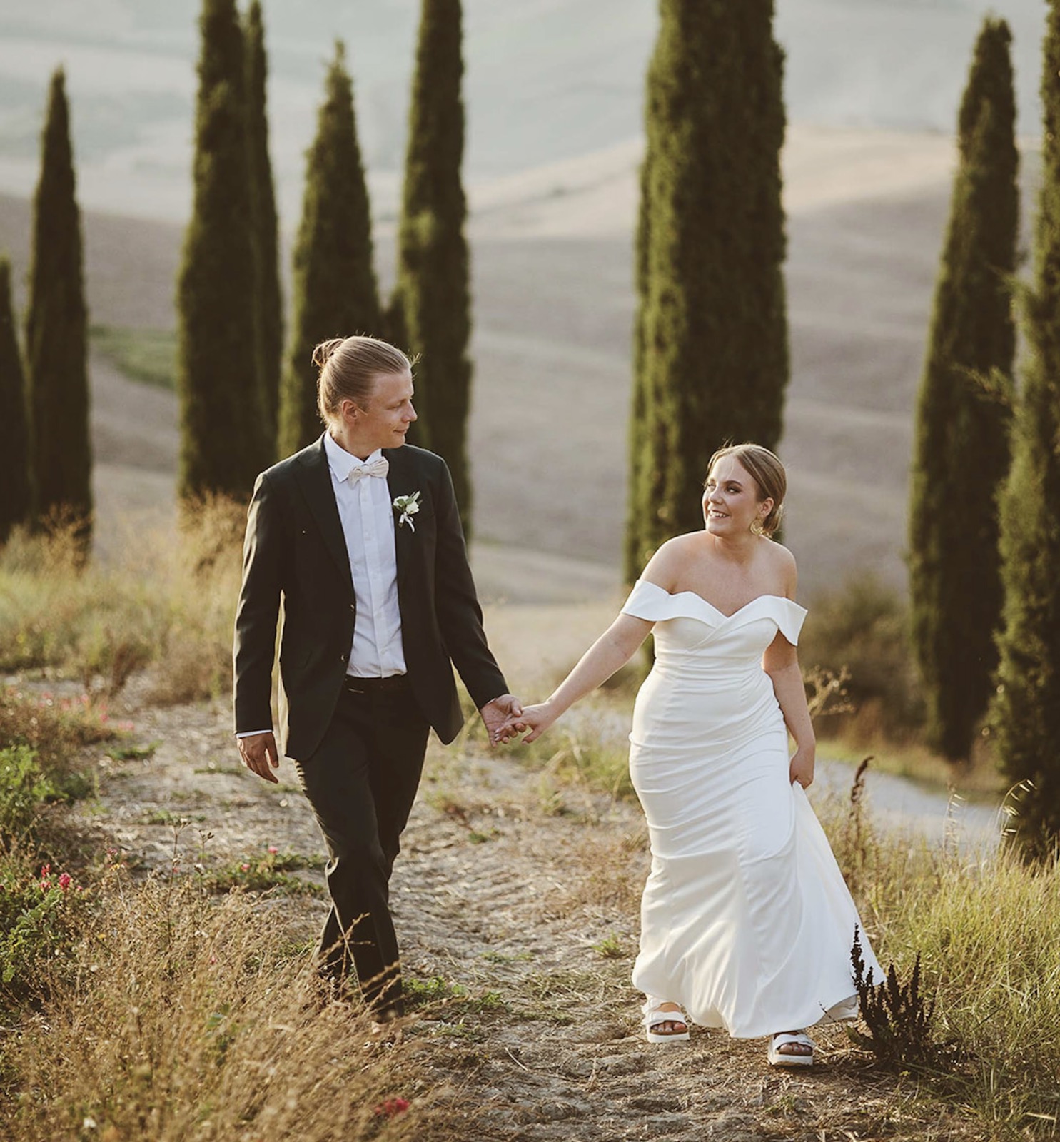 Kaisa and Paavo walking hand in hand along a cypress-lined path in the Tuscan hills