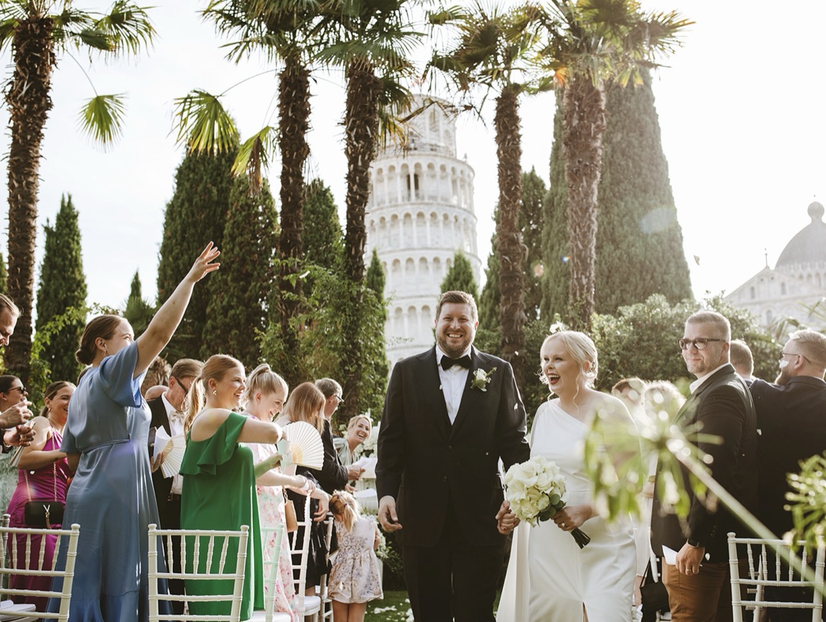 Nina and Fredrik walking through their ceremony garden with the Leaning Tower of Pisa behind them