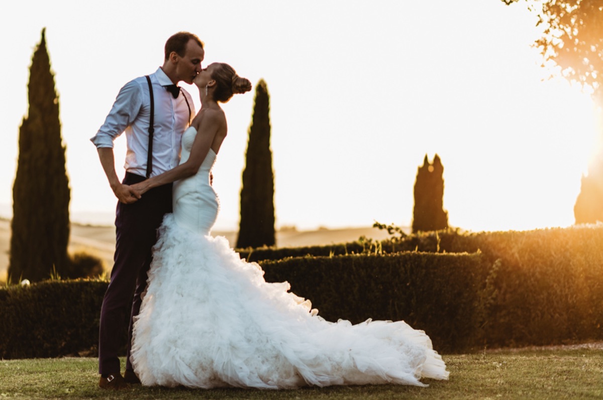 Bride and groom kissing at golden hour among cypress trees in the Tuscan countryside