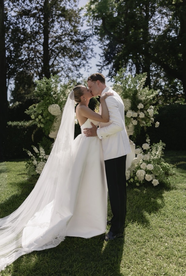 Bride and groom kissing at the altar, flanked by tall white floral arrangements